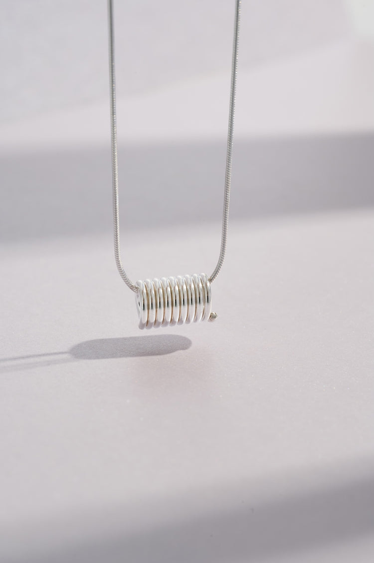 Sterling silver coil necklace on a 46-centimetre chain where the coil measures 13mm in length and 8mm in diameter and all inspired by Art Deco and minimalist architecture