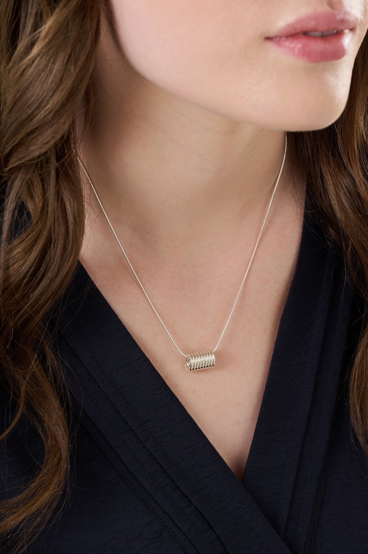 Sterling silver coil necklace with a 13mm long and 8mm wide coil on a 46 centimetre silver chain and worn over a dark blue blouse